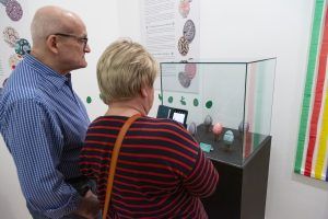 Zwiedzający wystawę „Górnośląskie kroszonki 2024” na tle gabloty z nagrodzonymi pracami